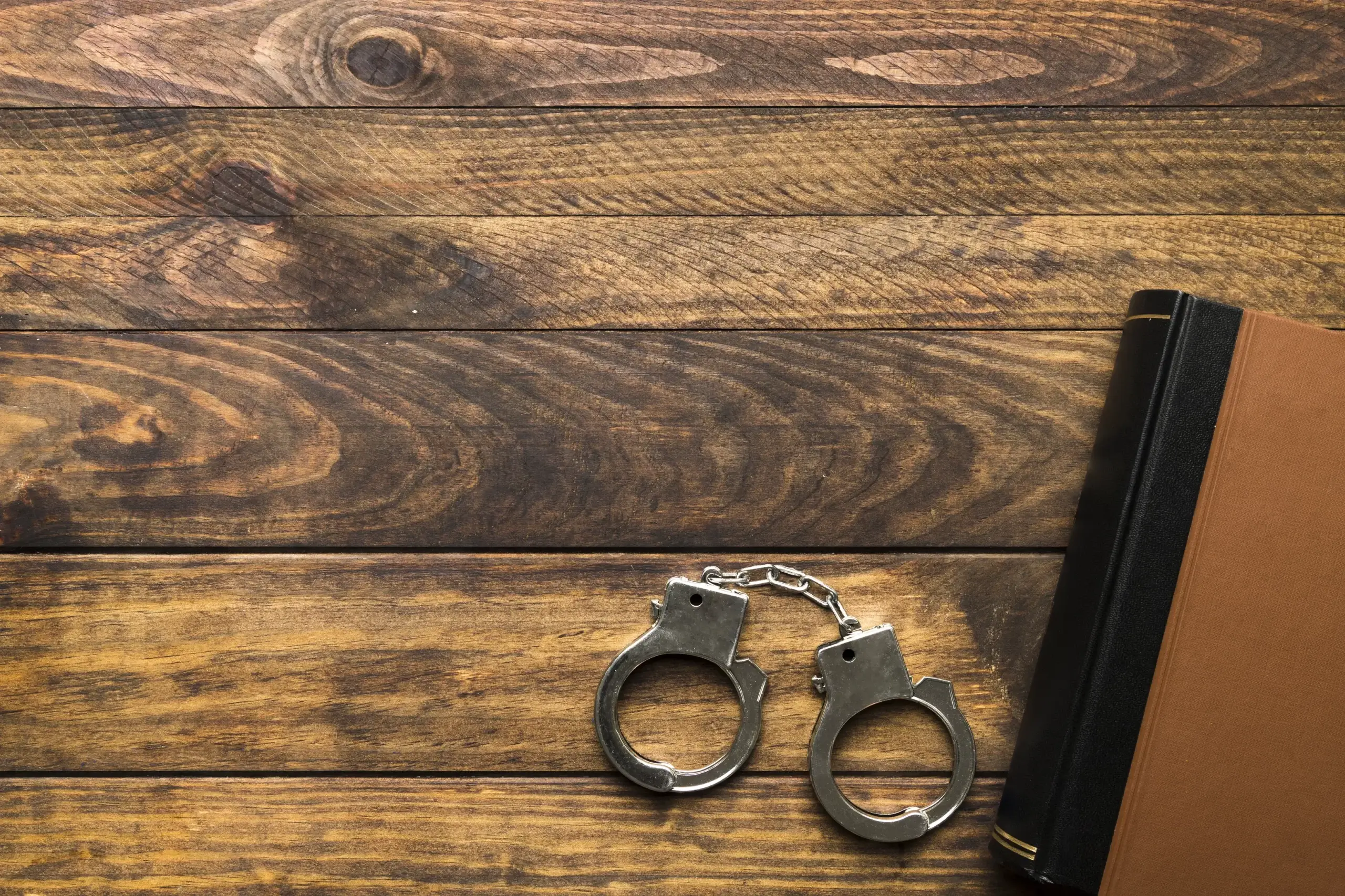 Law book and handcuffs on wooden table